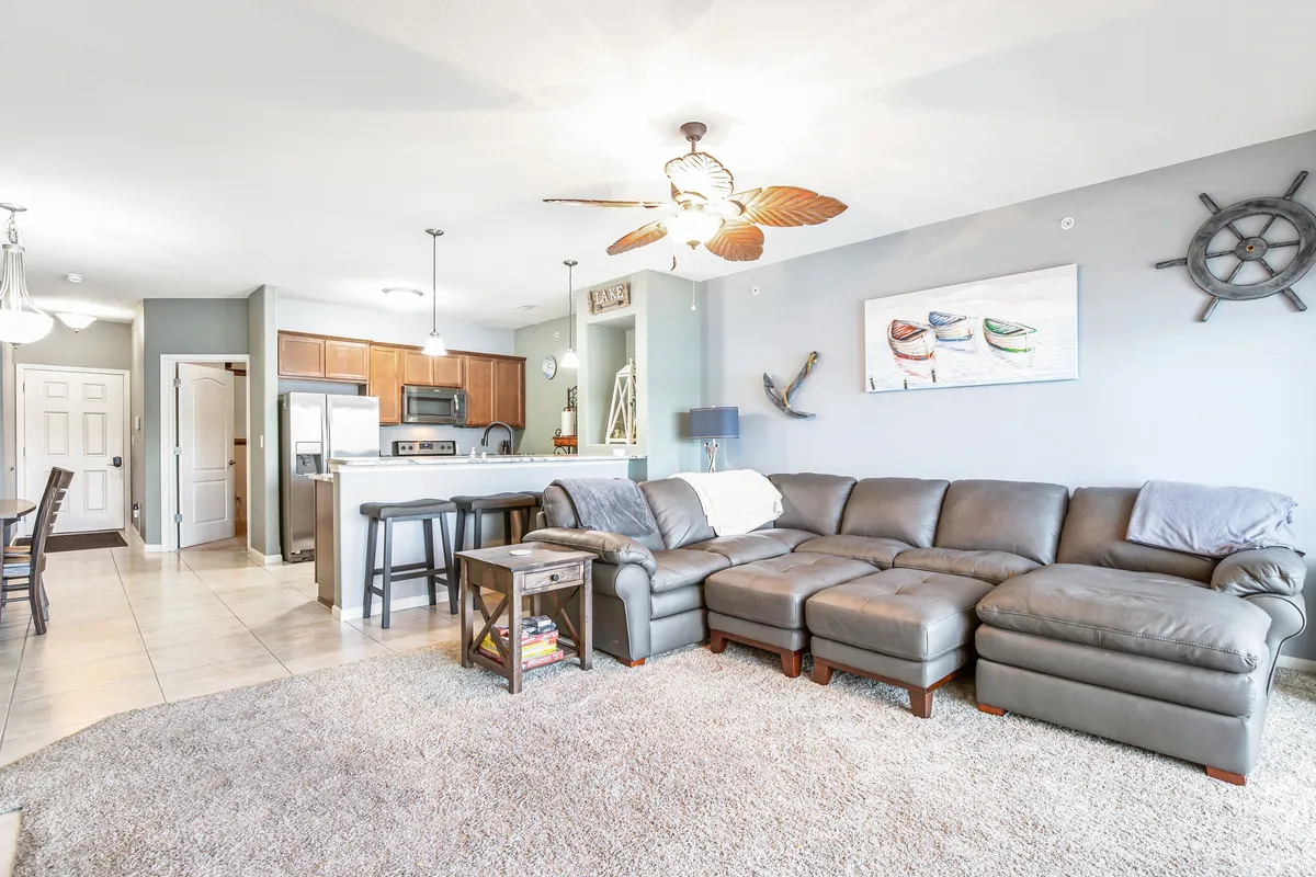 A welcoming open-concept living area featuring a plush leather sectional sofa, a view into the kitchen area, decorative wall art, and a ceiling fan overhead. The atmosphere encourages relaxation and togetherness, with plenty of space for family gatherings and cozy evenings indoors.