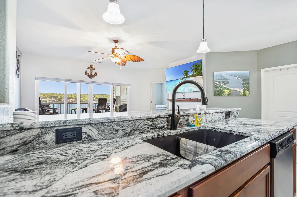 A bright kitchen with granite countertops, a large sink, and expansive windows offering lake views. The open layout and ceiling fan contribute to a relaxed, airy atmosphere.