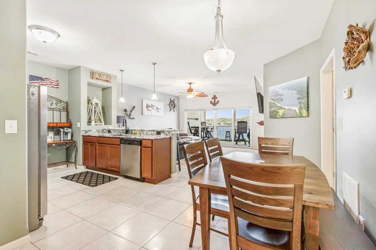 This interior scene features a kitchen island, dining table, and a window with a pleasant view, accented by decorative nautical elements. The layout visually connects the social heart of the condo with the exterior, suggesting both comfort and proximity to the scenic outdoors.