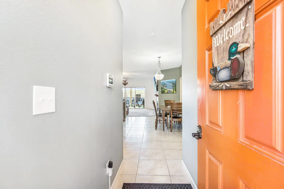 This image features a bright orange front door with a 'Welcome' sign, bathed in natural light, and offers a glimpse of the dining area beyond. The overall mood is warm and inviting, suggesting an immediate sense of arrival and hospitality.