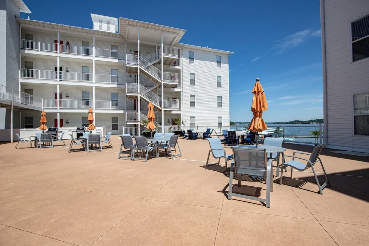 This exterior image captures the cheerful energy of the lakeside zero-entry swimming pool, with orange umbrellas, dining tables, and a sweeping view of the lake. The pool area looks inviting for groups to relax, socialize, and enjoy meals outdoors, all while overlooking the water.